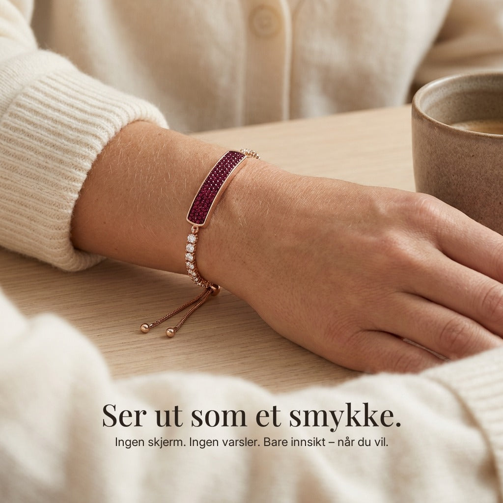 Selma Fitband i karminrosé på håndleddet ved en kaffekopp